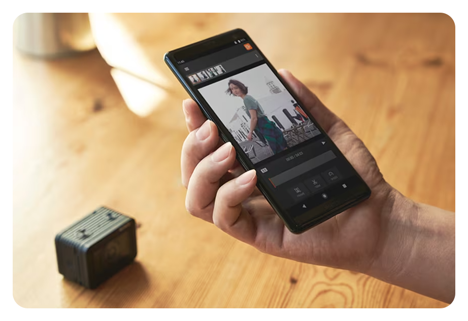 Person holding smartphone in hand above wooden table with sony rx0 ii